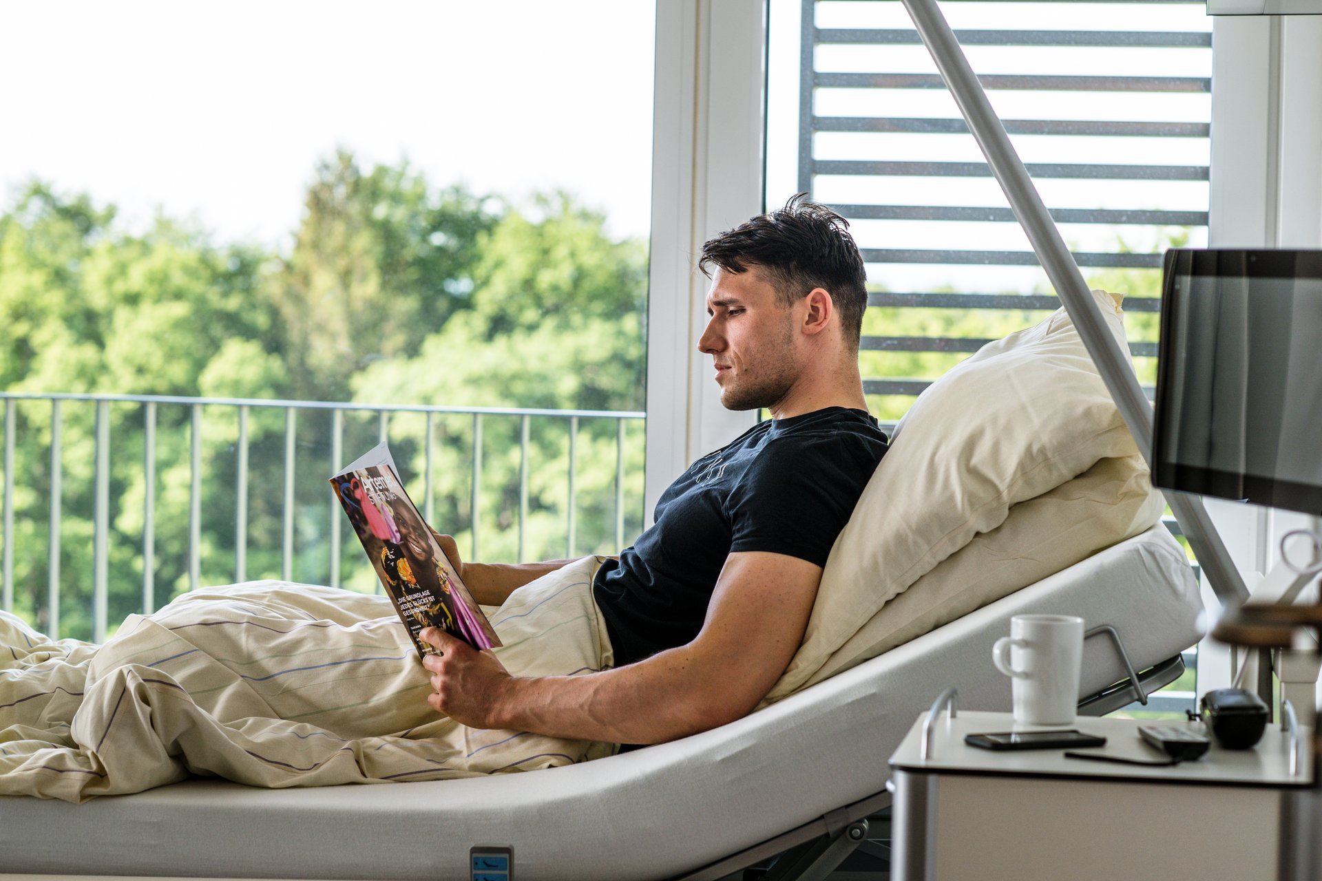 Ihr Aufenthalt - Mann sitzt in Pflegebett und liest in einem Buch